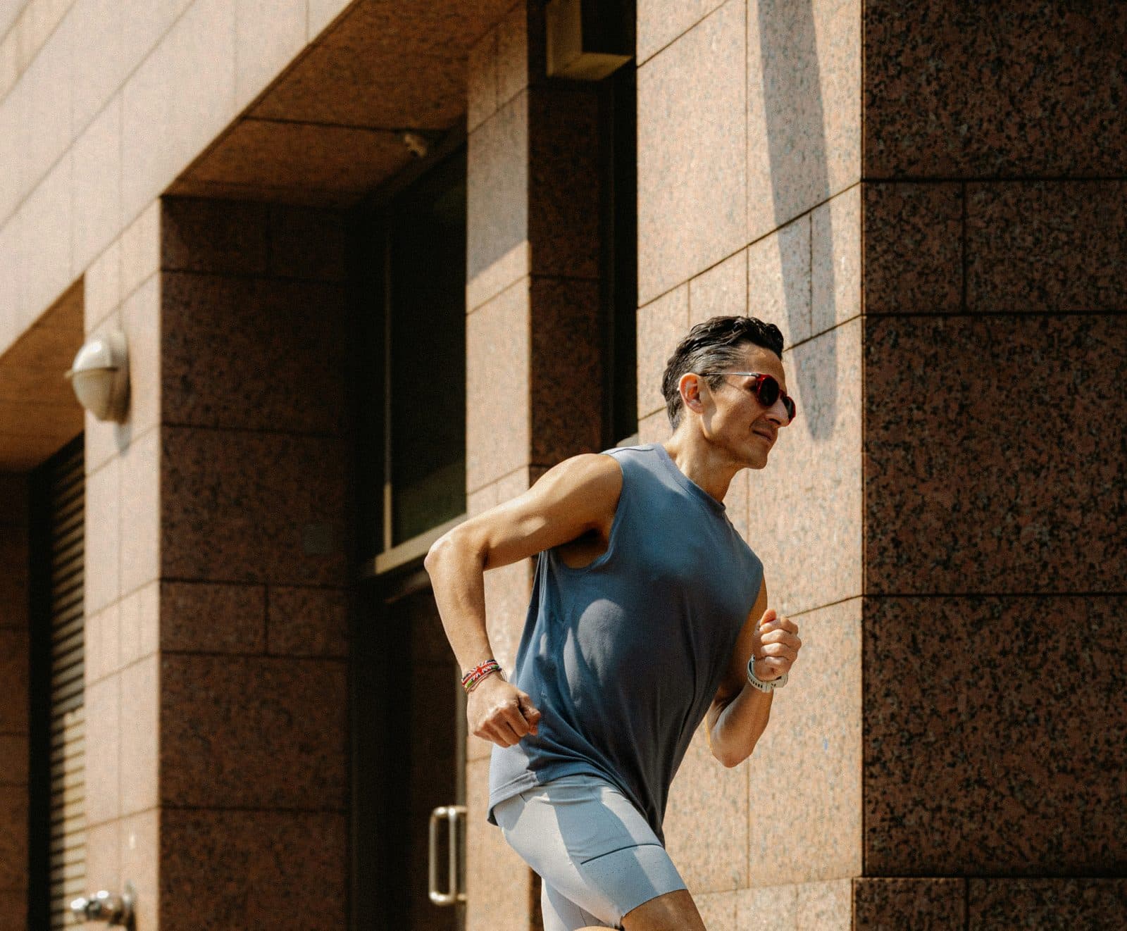 Man running in a grey-blue sleeveless training top and light grey shorts