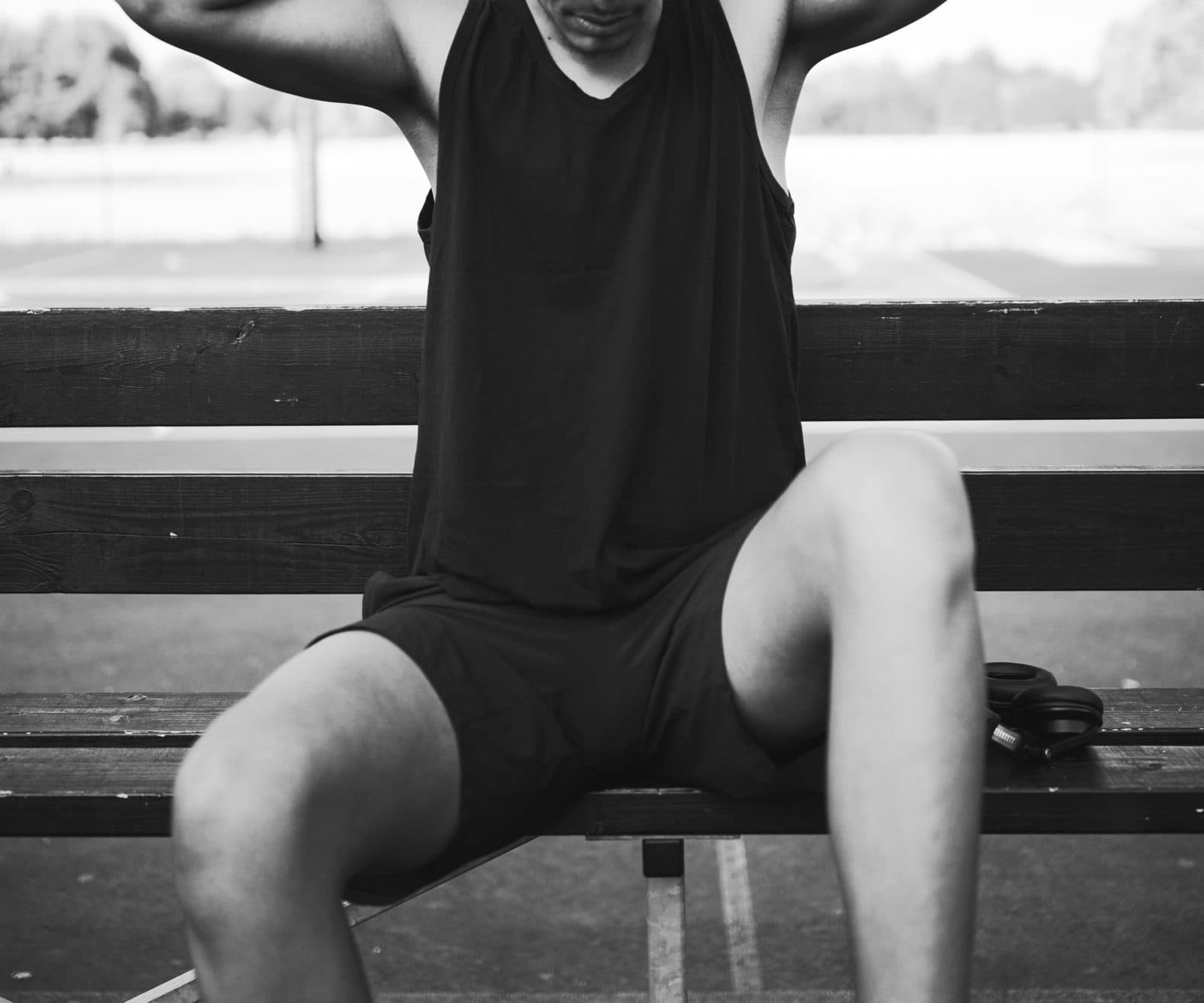 Man in a black sleeveless training tank and black shorts sitting on a bench