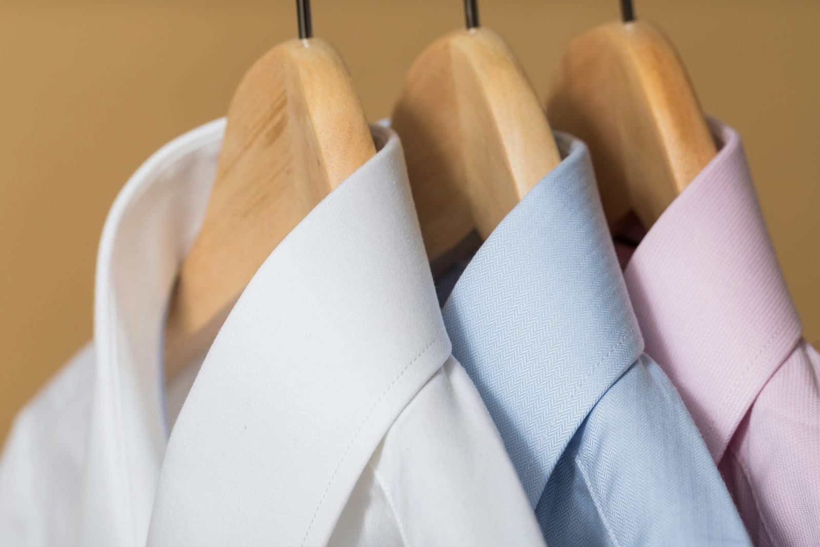 White, blue and pink dress shirts on wooden hangers