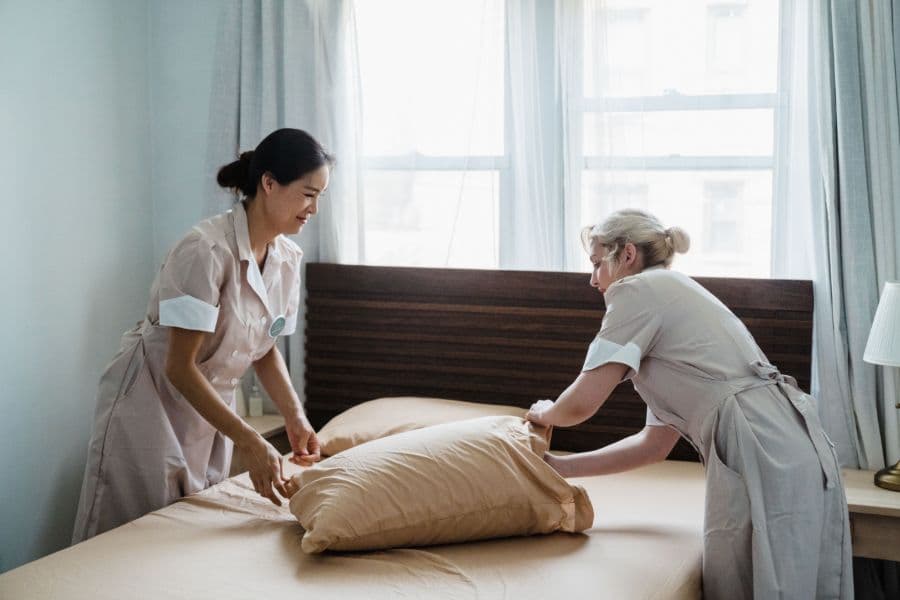 Housekeeping staff making up an institutional bed with plain poly-cotton linen