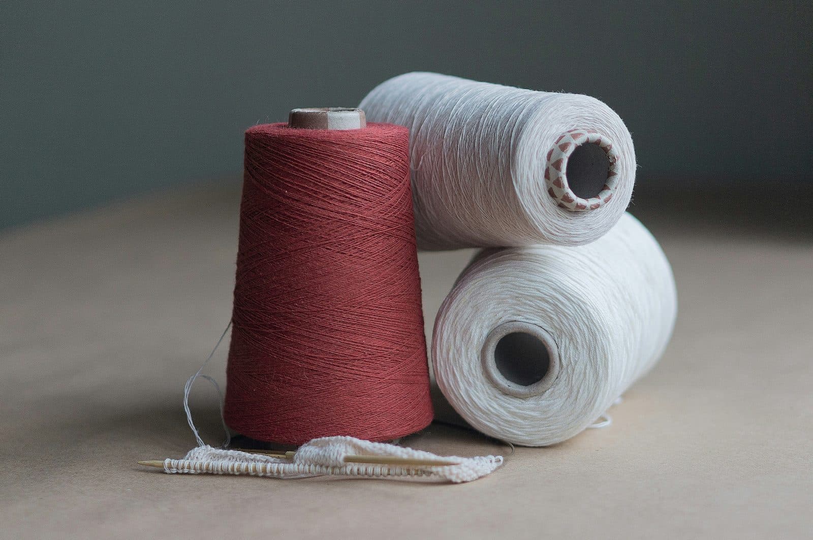 A red dyed cotton yarn cone beside two white yarn cones